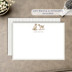 Puede incluir: Una tarjeta de papelería blanca con un borde gris fino, que presenta una ilustración en tinta marrón de dos perros y el nombre impreso JAMES KEUPER. La tarjeta está sobre un sobre a rayas grises y blancas, con el texto GIFT WRAP & A7 ENVELOPES INCLUDED.