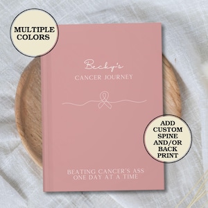 May include: A pink journal with the text "Becky's Cancer Journey" and a pink ribbon graphic. The text "Beating Cancer's Ass One Day At A Time" is printed on the bottom of the journal. The journal has a cream-colored background with the text "ADD CUSTOM SPINE AND/OR BACK PRINT" in black.