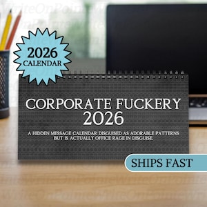 May include: A dark gray desk calendar for 2026 with the text "CORPORATE FUCKERY 2026". The calendar has a spiral binding and a blue starburst sticker that says "2026 CALENDAR". The text below reads "A HIDDEN MESSAGE CALENDAR DISGUISED AS ADORABLE PATTERNS BUT IS ACTUALLY OFFICE RAGE IN DISGUISE."