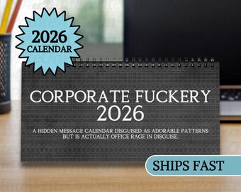 May include: A dark gray desk calendar for 2026 with the text "CORPORATE FUCKERY 2026". The calendar has a spiral binding and a blue starburst sticker that says "2026 CALENDAR". The text below reads "A HIDDEN MESSAGE CALENDAR DISGUISED AS ADORABLE PATTERNS BUT IS ACTUALLY OFFICE RAGE IN DISGUISE."