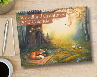 May include: A spiral-bound 2027 calendar titled Woodland Creatures 2027 Calendar, featuring a painted forest scene with a fox resting on a patterned rug near a large tree, two small rabbits in the grass, and soft golden sunlight filtering through.