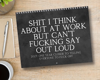 May include: A black wall calendar with white text that reads: SHIT I THINK ABOUT AT WORK BUT CAN'T FUCKING SAY OUT LOUD. Below this, smaller text reads: 2027: ONE YEAR CLOSER TO TELLING EVERYONE TO FUCK OFF. The calendar features a spiral binding at the top.