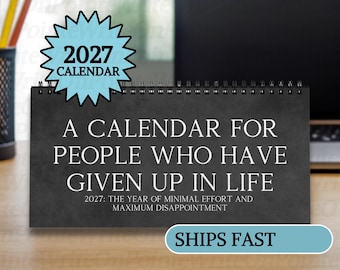 May include: A black spiral-bound desk calendar with white text that reads: A CALENDAR FOR PEOPLE WHO HAVE GIVEN UP IN LIFE. 2027: THE YEAR OF MINIMAL EFFORT AND MAXIMUM DISAPPOINTMENT. A light blue starburst graphic at the top displays 2027 CALENDAR.