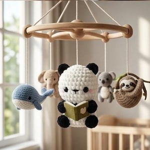 Può includere: Una giostrina per culla in legno con cinque animali in peluche lavorati all'uncinetto appesi a fili bianchi. Le figure includono una balena blu, un elefante beige, un panda centrale che legge un libro verde, un koala grigio e un bradipo.