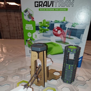 Puede incluir: Un set de acción Gravitrax Twist con 101 piezas y 2 elementos. El set incluye una torre verde y gris, una pieza de pista blanca y una pieza de pista verde y gris. El set está sobre una superficie de baldosas hexagonales grises y blancas.