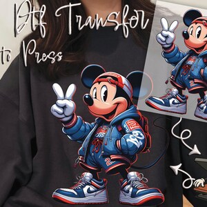 May include: DTF Transfer, Ready to Press. A cartoon illustration of Mickey Mouse wearing a blue jacket, shorts, and sneakers, making a peace sign. The design includes a red and white baseball cap and a backpack. The image is on a white background.
