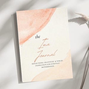 Könnte beinhalten: Ein Journal mit einem Aquarelldesign. Das Cover zeigt Pfirsich- und Cremetöne mit den Worten "the Ima Journal" in eleganter Schrift. Der Untertitel des Journals lautet "Reflections, Gratitude & Torah Inspiration for Everyday Motherhood."