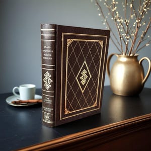 May include: A hardcover book with a dark brown cover and gold accents. The book's spine features the names Plato, Epictetus, Marcus Aurelius, and the text "The Harvard Classics Collector's Edition." The cover has a diamond pattern with gold trim.