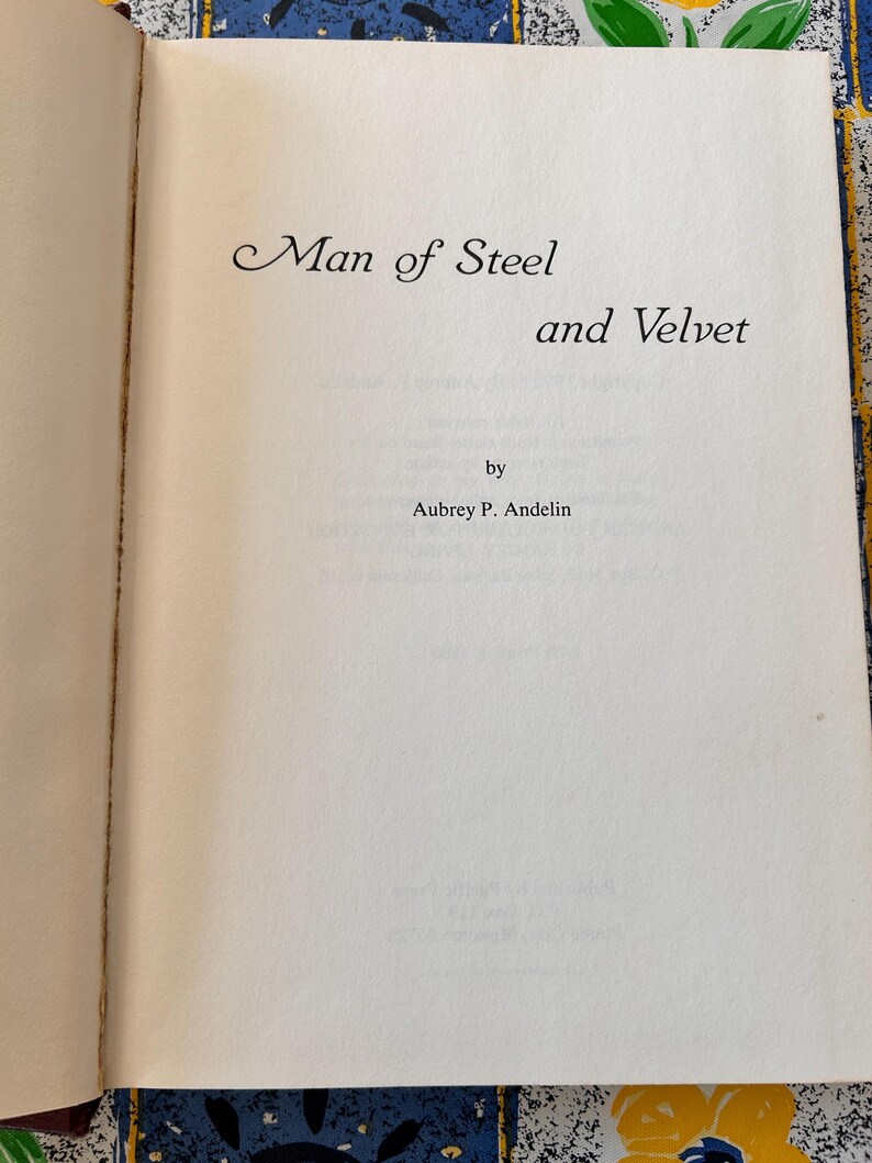 Op de afbeelding: Open boek met de titel "Man of Steel and Velvet" in sierlijke letters. De naam van de auteur, Aubrey P. Andelin, staat eronder. De pagina's zijn gebroken wit met lichtgele randen.
