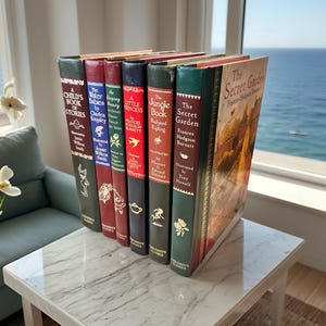 May include: A collection of classic books with colorful spines, including titles like "The Secret Garden" and "The Jungle Book," are arranged on a white marble table. The books are displayed near a window with a view of the ocean.