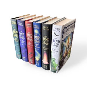 Puede incluir: Una colecci&oacute;n de seis libros de tapa dura de Chris Colfer, titulados "The Land of Stories". Las lomos de los libros son de varios colores: verde, morado, rojo, azul, negro y blanco. El t&iacute;tulo y el autor son visibles.