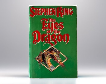 May include: A green hardcover book with the title "The Eyes of the Dragon" by Stephen King. The cover features a red dragon with gold accents.