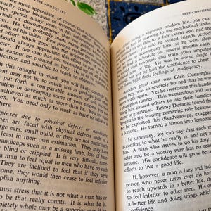 Op de afbeelding: Open boek met tekst over zelfvertrouwen en persoonlijke ontwikkeling. De vergeelde pagina's bevatten tekst over uitdagingen en het bereiken van doelen. De tekst is in zwarte letters.