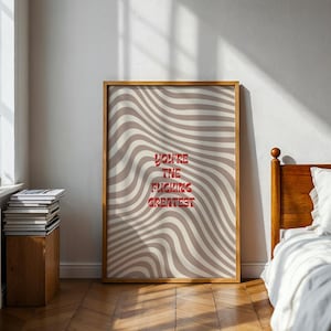 Könnte beinhalten: Ein gerahmter Kunstdruck mit einem wellenförmigen beige-weißen Muster. Der rote Text lautet "YOU'RE THE FUCKING GREATEST". Der Druck wird in einem Raum mit Holzboden und einem Bett ausgestellt.