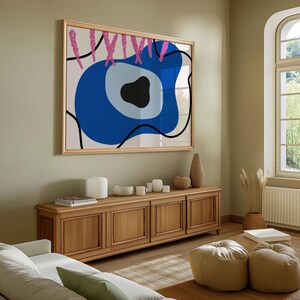 Könnte beinhalten: Ein großes, gerahmtes abstraktes Kunstwerk mit einem blauen, schwarzen und rosa Design hängt über einem Holzschrank. Das Kunstwerk zeigt eine kräftige blaue Form mit einem schwarzen Zentrum und rosa Akzenten. Der Schrank ist mit dekorativen Gegenständen gefüllt.