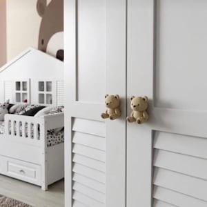 May include: White cabinet doors with two small, tan teddy bear knobs. The doors have a shutter design. A white house-shaped bed frame and a bear wall decal are visible in the background.