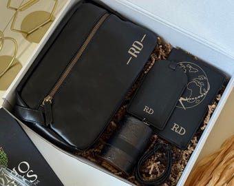 May include: A black gift box containing a black travel bag, passport holder, luggage tag, and a candle. The items have gold accents and the initials "RD-". The passport holder features a world map design.