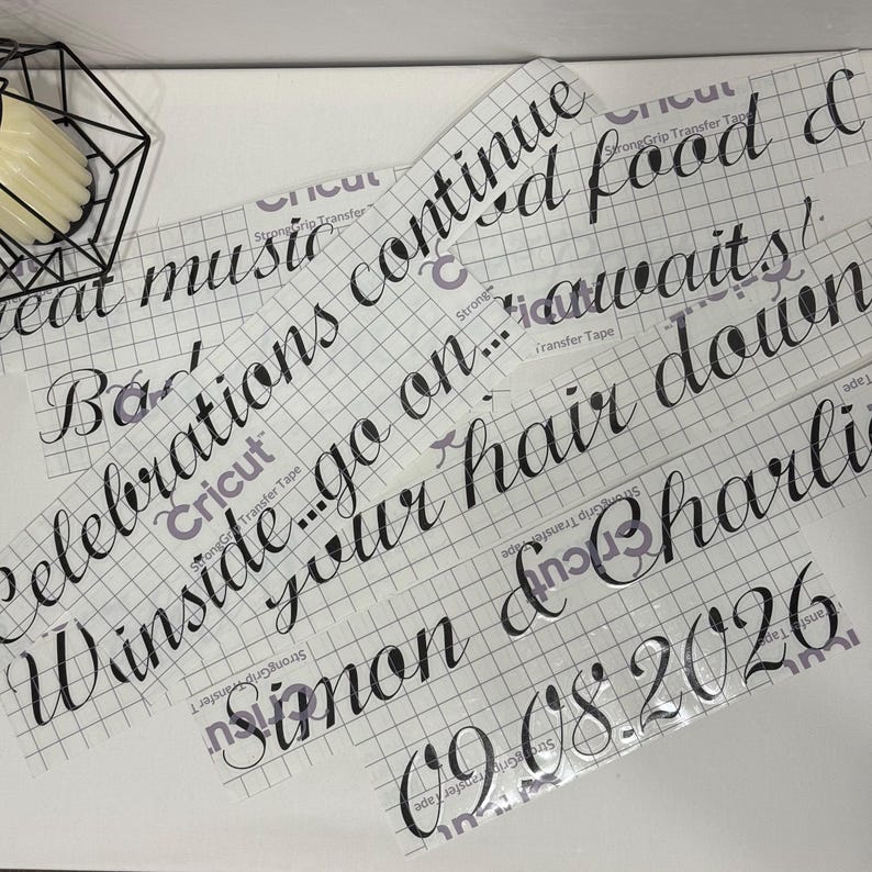 May include: Black vinyl lettering decals on clear transfer tape with a grid pattern. The text reads: Great music, good food & celebrations continue... go on... winside your hair down, Simon & Charlie, 09.08.2026. The decals feature a cursive script font.