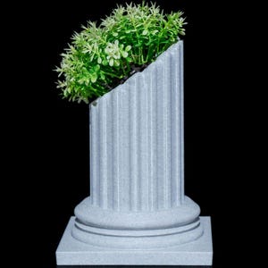 May include: A gray, fluted column-shaped planter with a square base, holding a vibrant green plant. The top of the planter is cut at an angle, creating a unique design. The plant has small, light green leaves.