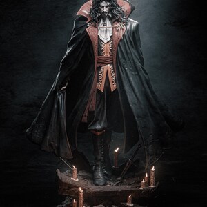 May include: A dark-haired figure in a black cape and red and gold clothing stands on a rocky base with lit candles. The figure has a serious expression and appears to be a vampire.