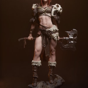 May include: A detailed statue of a warrior woman, clad in brown leather armor and fur accents. She holds a large battle axe and stands on a rocky base. The statue features intricate details, including a skull shoulder piece and fur-lined boots.