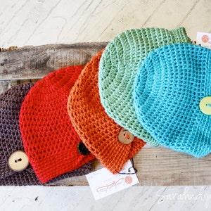 May include: Four crocheted hats in different colors, including brown, orange, green, and blue, with a button on each hat. The hats are arranged on a wooden surface.