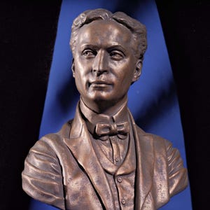 Könnte beinhalten: Eine Bronzestatue von Harry Houdini, einem berühmten Magier und Entfesselungskünstler. Die Büste steht auf einem Sockel mit der Aufschrift "HOUDINI".