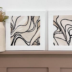 May include: Two framed abstract paintings with black lines on a beige background. The paintings are hung on a wall above a brown mantel.