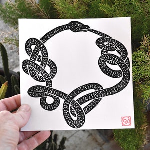 May include: Black and white print of a snake forming a circle with its head biting its tail. The snake is patterned with a series of small, wavy lines.