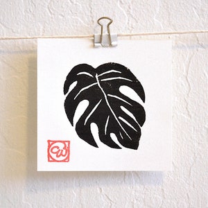 May include: Black and white print of a monstera leaf with a red stamp in the lower left corner that says "CW".