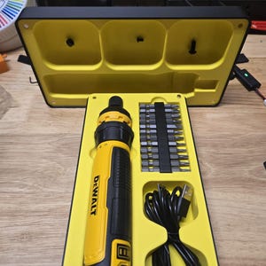 Puede incluir: Un kit de destornillador inalámbrico DeWalt amarillo y negro. El kit incluye un destornillador, un juego de puntas y un cable de carga USB. El destornillador y el kit están alojados en una caja amarilla y negra.