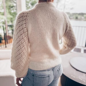 Peut inclure: Un pull en tricot blanc avec un motif de dentelle délicat sur les manches. Le pull est doux et moelleux, et les manches sont longues et fluides.