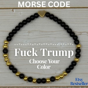 May include: A beaded bracelet with black and gold beads, featuring a gold heart charm. The text "Fuck Trump" and "Choose Your Color" are displayed on the image. The words "Morse Code" are at the top.