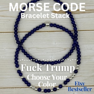 May include: Two beaded bracelets in navy blue and silver. The top bracelet is a continuous loop, while the bottom bracelet has a message spelled out in Morse code. Text on the image reads "Morse Code Bracelet Stack" and "Fuck Trump Choose Your Color".