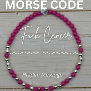 May include: A beaded bracelet with a hidden message. The bracelet features bright pink beads and silver-colored accents. The text "MORSE CODE" and "Fuck Cancer" are displayed, along with a Morse code sequence and the words "Hidden Message".