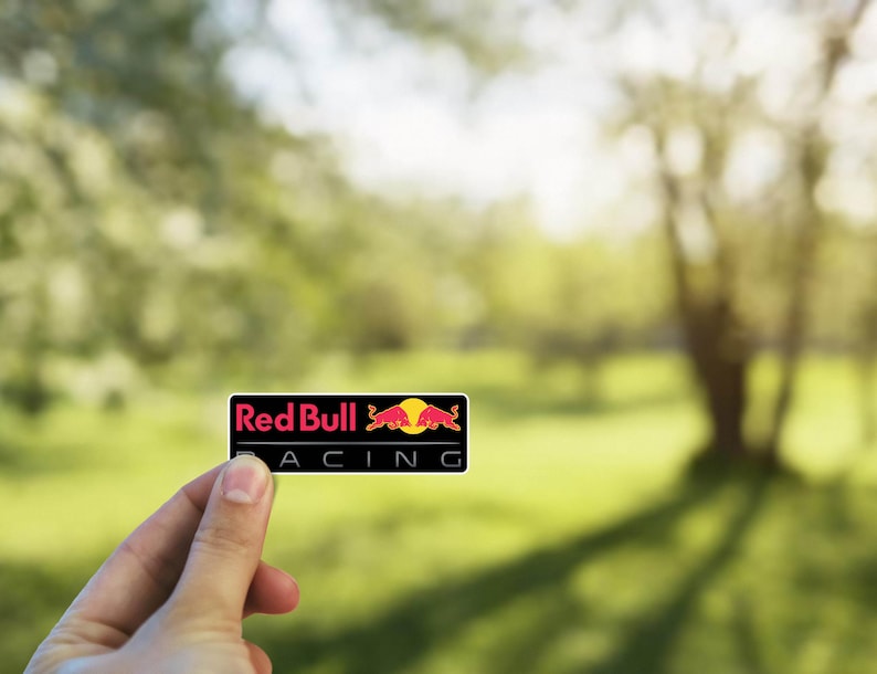 以下が含まれることがあります： 「Red Bull Racing」というテキストと赤い雄牛のロゴが入った黒と赤のステッカーです。