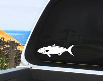 May include: A white silhouette of a fish on a black background. The fish is facing right and has a slightly curved body. The fish is on a truck's rear window.