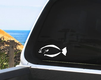 May include: White vinyl decal of a halibut fish silhouette on a black truck window. The truck is parked in front of a beach scene.