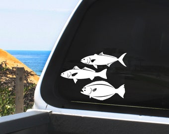 May include: White vinyl decal featuring three stylized fish silhouettes. The fish are arranged in a diagonal pattern, with varying shapes and sizes. The decal is applied to a vehicle window, with a coastal background visible.