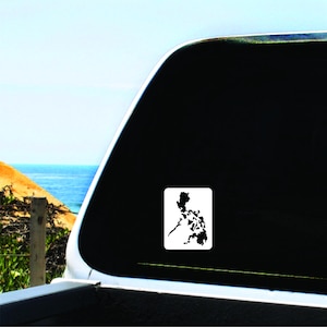 May include: A rectangular white sticker featuring a black silhouette of the Philippines map. The sticker is affixed to a vehicle window, with a backdrop of the ocean and sky.