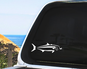 May include: White silhouette of a fish on a black truck window. The fish is facing right and has a long, thin body with a pointed head.