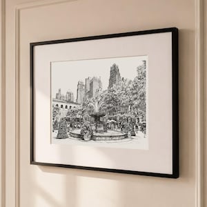 May include: A black and white ink drawing of a city park scene featuring a central fountain, surrounding trees, and tall skyscrapers in the background. The artwork is presented in a simple black frame with a wide white mat border.
