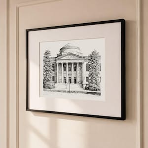 Op de afbeelding: Zwartgelijste kunstdruk van een gebouw met een koepelvormig dak en zuilen. De zwart-wit tekening toont de gevel van het gebouw, met bomen aan weerszijden. Het kunstwerk wordt tentoongesteld op een cr&egrave;mekleurige muur.