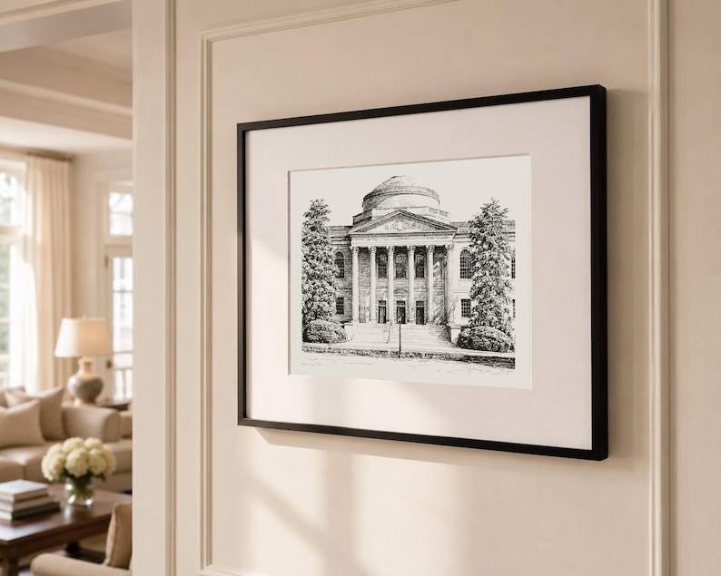 Op de afbeelding: Zwartgelijste kunstdruk van een gebouw met een koepelvormig dak en zuilen. De zwart-wit tekening toont de gevel van het gebouw, met bomen aan weerszijden. Het kunstwerk wordt tentoongesteld op een cr&egrave;mekleurige muur.