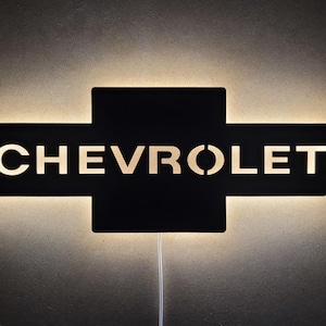 Może przedstawiać: Czarna metalowa lampa ścienna z wyciętym logo Chevrolet. Lampa jest oświetlona, dając ciepłe światło.