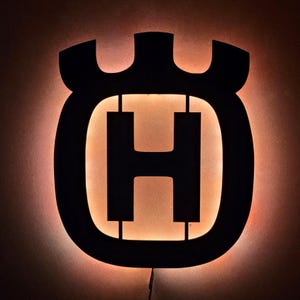 Könnte beinhalten: Schwarz-weiße Silhouette des Husqvarna-Logos mit einem hellbraunen Schein dahinter.