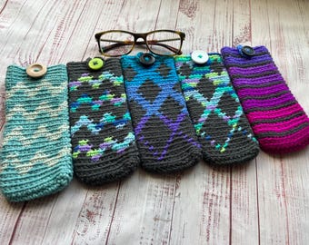 May include: Five handmade crochet eyeglass cases in various colors and patterns. The cases are teal, black with blue and green accents, black with blue and purple accents, black with teal and purple accents, and purple and pink striped. Each case has a button closure.