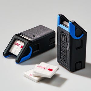 Puede incluir: Dos dispositivos rectangulares negros y azules con un acabado texturizado, posiblemente impresos en 3D, y pequeños cuadrados blancos con marcas rojas. Los dispositivos tienen un diseño único con tapas anguladas y detalles azules.