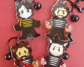 May include: Four acrylic keychains featuring cartoon characters in black military-style jackets with red accents. Each character has animal ears and paw-shaped hands. The keychains include black metal rings and small black bells attached to the top.