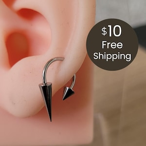 May include: A silver-toned horseshoe-shaped earring featuring two pointed cone-shaped spikes at each end. The jewelry is displayed on a flesh-toned ear model. The design consists of a curved metal bar with a larger spike on one side and a smaller spike on the other.